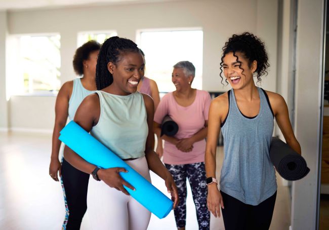 Several women walking with rolled up yoga mats while talking and smiling